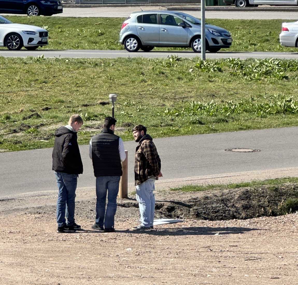 Geologe erklärt zwei jungen Männern iwe man einen GNSS-Stab verwendet, um Checkerboards einzumessen.